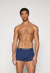 Námornícke modré bavlnené boxerky s elastickým pásom s logom s nápisom "GUESS" v bielej a červenej farbe. Hladká textúra, priliehavý strih.