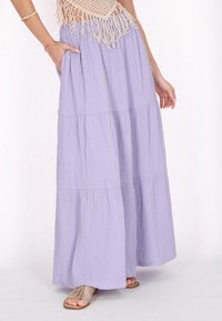 Maxiskirt i lys lavendel krinklet stof, lagdelt design, med sidelommer og en let silhuet, parret med metalfarvede sandaler.