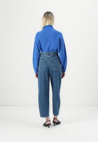 Maglione blu lavorato a maglia con colletto alto sovrapposto a jeans in denim blu a vita alta. I jeans hanno tasche posteriori e un taglio dritto.