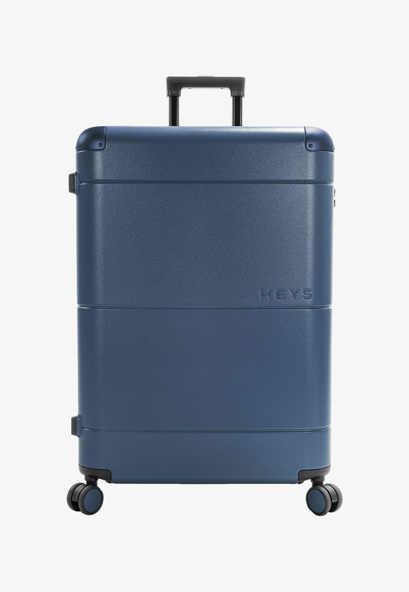 Valise rigide bleu marine avec quatre roues pivotantes et une poignée télescopique, nom de marque "HEYS" en relief à l'avant.