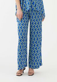 Pantalon bleu à motifs en tissu lisse, avec un design géométrique agrémenté de touches de vert et de blanc. Coupe large et taille haute.