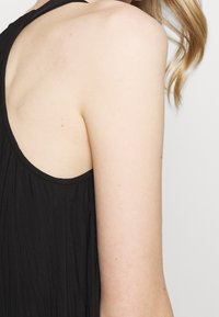 Mustat hihattomat yläosat, joissa on kellotettu muotoilu, pehmeä kangas ja leveä kaula-aukko, sekä laskostusdetaljit selkäpuolella.