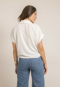 Un chemisier blanc à manches courtes avec une coupe décontractée, un col et une texture douce, associé à un jean bleu taille haute à jambes larges.