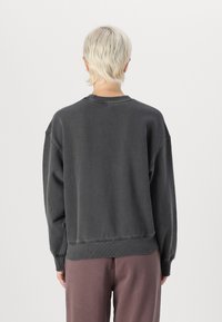 Donkergrijze oversized sweatshirt met geribde halslijn en boorden, met een zachte textuur en een ontspannen pasvorm. Achteraan zijn de verlaagde schouders zichtbaar.
