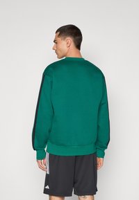 Grøn sweatshirt lavet af tekstureret stof, med sorte sidelister, rund hals og ribbede manchetter og kant. Bæres med sorte shorts.