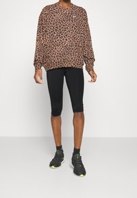 Sudadera con estampado de leopardo en marrón y negro, con mangas largas y cuello redondo, combinada con leggings capri negros y zapatillas negras.