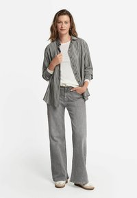 Randig skjorta i grått och vitt, lagd över en vit t-shirt. Bärs med grå vida jeans och beige skor. Avslappnad outfit.