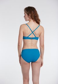 Bikini set v teal barvi z zasnovo prepletenega hrbta, nastavljivimi naramnicami in nizkim pasom. Gladka tekstura, minimalni dodatki.