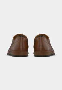 Braune Lederschuhe zeichnen sich durch eine glatte Oberfläche, eine abgerundete Zehenpartie, gestickte Details und einen stabilen Holzabsatz aus. Das Design ist schlank und minimalistisch.
