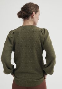 Olivno zelena pletena pulover s pufastimi rokavi, ki ima teksturiran pikčast vzorec ter rebraste manšete in rob. Gladek material.