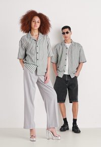 Camicie a maniche corte rigate in verde e bianco, pantaloni a gamba larga grigi e pantaloni corti neri; le scarpe del modello sono tacchi a piattaforma argento.
