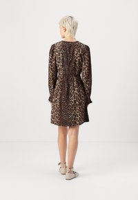 Vestido de padrão de leopardo com mangas longas, parte de trás franzida e bainha evasé. Feito de um tecido suave; apresenta punhos com babados e detalhes ajustáveis com laços.