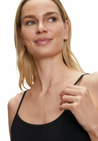Czarny top na ramiączkach z cienkimi paseczkami, o miękkiej i gładkiej fakturze. Modelka ma jasną karnację i długie blond włosy, lekko zwrócona w bok.