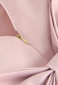 Gaiši rozā audums ar gludu tekstūru, ar paslēptu iestrādājamu rāvējslēdzēju ar zelta vilkšanas cilpu un mezglu detaļu stūrī.