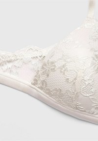 Lace bralette in light beige featuring floral patterns and a textured design. Soft satin band and adjustable straps.