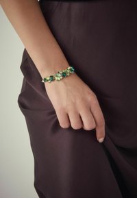 Gold-tone bracelet featuring green and blue gemstones of varying sizes and shapes, with a textured design and intricate metal accents.