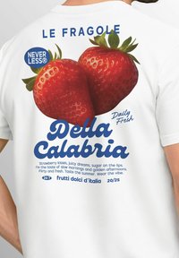 Weißes T-Shirt mit einem großen Grafikdruck von zwei roten Erdbeeren, blauer Schrift, die "Della Calabria" bewirbt, und dekorativer Typografie.