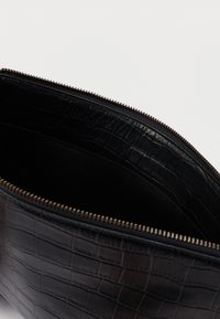 Pochette en cuir noir embossé crocodile avec fermeture éclair. L'intérieur présente une doublure noire lisse et des détails subtils de texture.