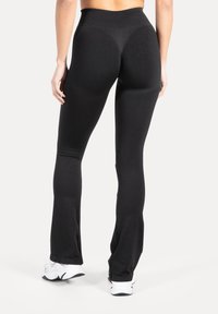 Zwarte legging met hoge taille en uitlopende pijpen, gladde textuur en rekbare stof. Geen zichtbare patronen of metalen details.