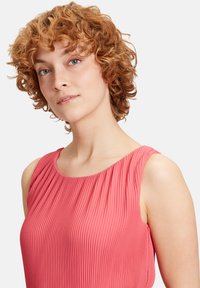 Rosa plisset top med rund halsudskæring og ærmeløs design, der har en glat tekstur og bløde draperingsdetaljer.