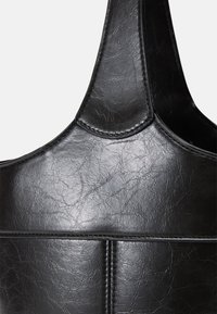 Μαύρη τσάντα χειρός φτιαγμένη από υφασμάτινη ψεύτικη δέρμα. Διαθέτει καμπυλωτούς χειρολαβές και ορατές ραφές κατά μήκος των ραφών με λεία επιφάνεια.