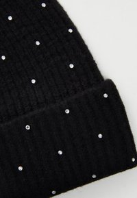 Beanie nera lavorata a maglia con texture a coste, decorata con dettagli di accenti simili a cristalli sparsi. Materiale morbido, design pieghevole.