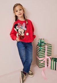 Punane kapuutsiga sweatshirt, millel on sädelev Minnie Mouse'i disain, koos siniste teksade ja sädeleva tossudega. Taustal rohelised ja roosad triibulised kinkekotid.