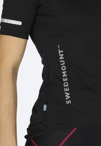 Svart atletisk tröja med korta ärmar, med reflexdetaljer, "SWEDEMOUNT"-logotyp och en liten svensk flagga.