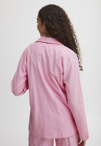 Light pink, long-sleeve shirt with a collar, featuring a loose fit and textured fabric. Includes buttoned cuff detail on the sleeve.