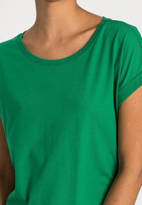 Groen T-shirt met korte mouwen, gemaakt van zacht stof, met een ronde hals en subtiele stikseldetails langs de kraag en mouwen.