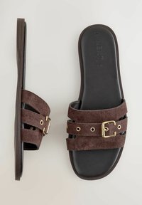 Sandalias deslizantes de ante marrón con dos correas y hebillas en tono dorado, una suela plana de goma negra y un acabado interior suave.