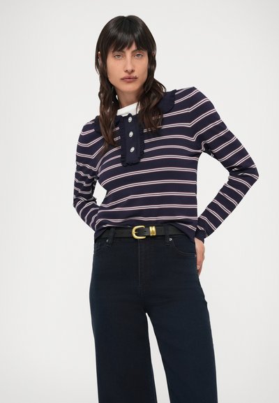 Laevastiku triibuline pika varrukaga pluus volangidega krae, nööpidega kaelusel, ühendatud tumedate teksade ja musta vööga, millel on kuldne pandl.