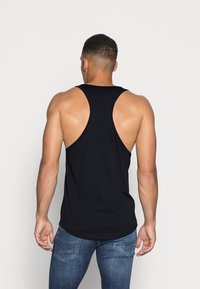Svart tank topp med brede armhull, laget av mykt stoff. Har en buet kant og en tettsittende design, sett bakfra.