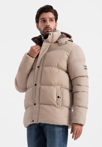 Beige vadderad jacka med dragkedja och knappstängning, med en snodd för huven och rutigt foder, två framfickor och ribbade muddärmar.