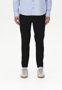 Black tapered pants with a streamlined fit, paired with light gray sneakers and a blue button-up shirt. Simple, clean design without patterns.