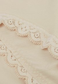 Beige tyg med en slät yta, försedd med krämfärgad spetskant med scalloped kanter och delikata blommönster längs ena sidan.