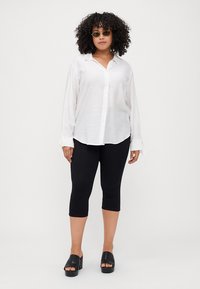 White long-sleeve button-up shirt with cuffs, black capri leggings, and black platform sandals. The shirt features a smooth, lightweight fabric.