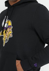 Felpa nera con cappuccio caratterizzata da un grande logo dei Vikings sul davanti, con tasca frontale e accento viola sulle maniche. Realizzata in materiale misto cotone.