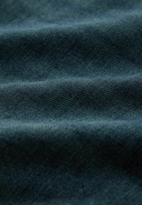 Tumši zilas džinsa audums ar strukturētu virsmu, kas izceļ smalku virpuļa rakstu un redzamas šuves krokās.