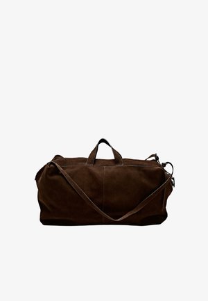 Hnědá semišová taška typu duffel s dvojitými držadly a odnímatelným ramenním popruhem. Má minimalistický design a viditelné švy podél spár.