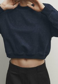 Laivastonsininen lyhyt collegepaita farkkukankaasta, jossa on resorikääntö kaulassa ja helmassa. Pinta on teksturoitu ja istuvuus rento, yhdistetty tummiin alaosiin.