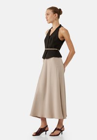 Zwarte mouwloze top met een V-hals en een ceintuurtje in de taille, gecombineerd met een vloeiende beige midi-jurk en bruine haksandalen. Eenvoudige ontwerpelementen.