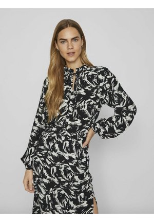 Robe à motifs noir et blanc avec des manches longues, un col haut et un détail en forme de trou de serrure à l'avant. Tissu doux et fluide avec une coupe décontractée.