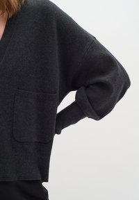 Mörkgrå ulltröja med djup V-ringning, vida ärmar och en framficka, med en mjuk textur och kort längd.