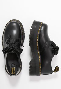 Scarpe stringate in pelle nera con suola spessa e rigata e cuciture gialle. Presentano lacci in satin e un'etichetta con logo sul tallone.