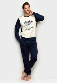 Pantaloni della tuta blu navy abbinati a una felpa girocollo, con una maglia color crema con la scritta "Après Ski Social Club" e polsini a coste.