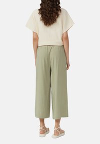 Haut crème à manches courtes associé à un pantalon large vert clair. La tenue présente une coupe décontractée et une texture douce. Les chaussures comprennent des sandales beiges.