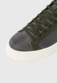 Gray textile sneaker with olive green leather accents, featuring a rounded toe and white rubber sole. Laces are matching green.