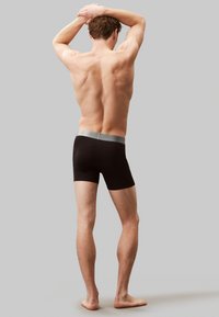 Boxers noirs avec une ceinture grise, fabriqués en tissu lisse, s'ajustant parfaitement, de longueur mi-cuisse et sans motifs visibles.