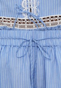 Robe à fines rayures bleu et blanc avec un galon en dentelle et deux nœuds noués en tissu à la taille et à l'encolure.